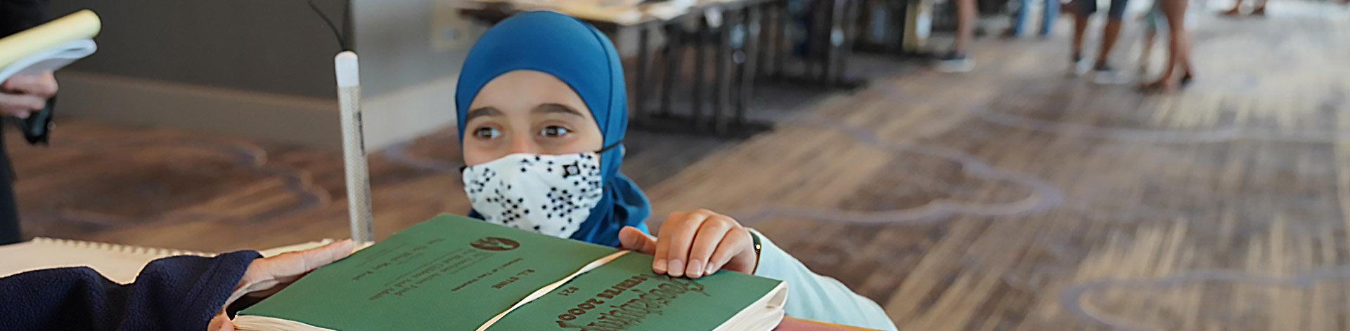 A young blind girl reaches up to read the title of a Braille book.