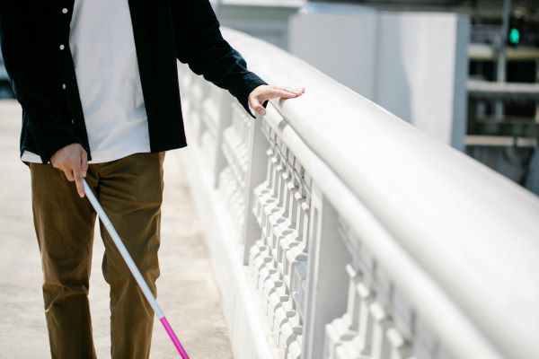 A person using a white cane walks along a city sidewalk, focussing on independence and guidance.  